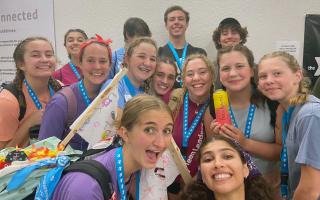 A group of teens wearing blue lanyards gather for a photo. All 12 people have big smiles.
