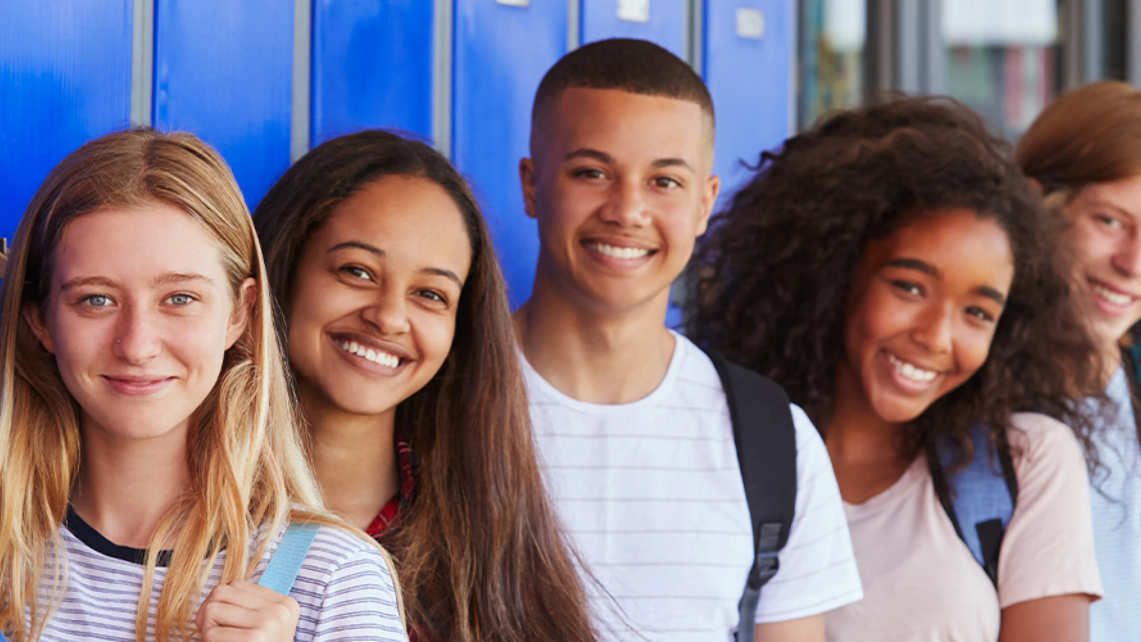 teens wearing backpacks smiling and standing in front of blue lockers