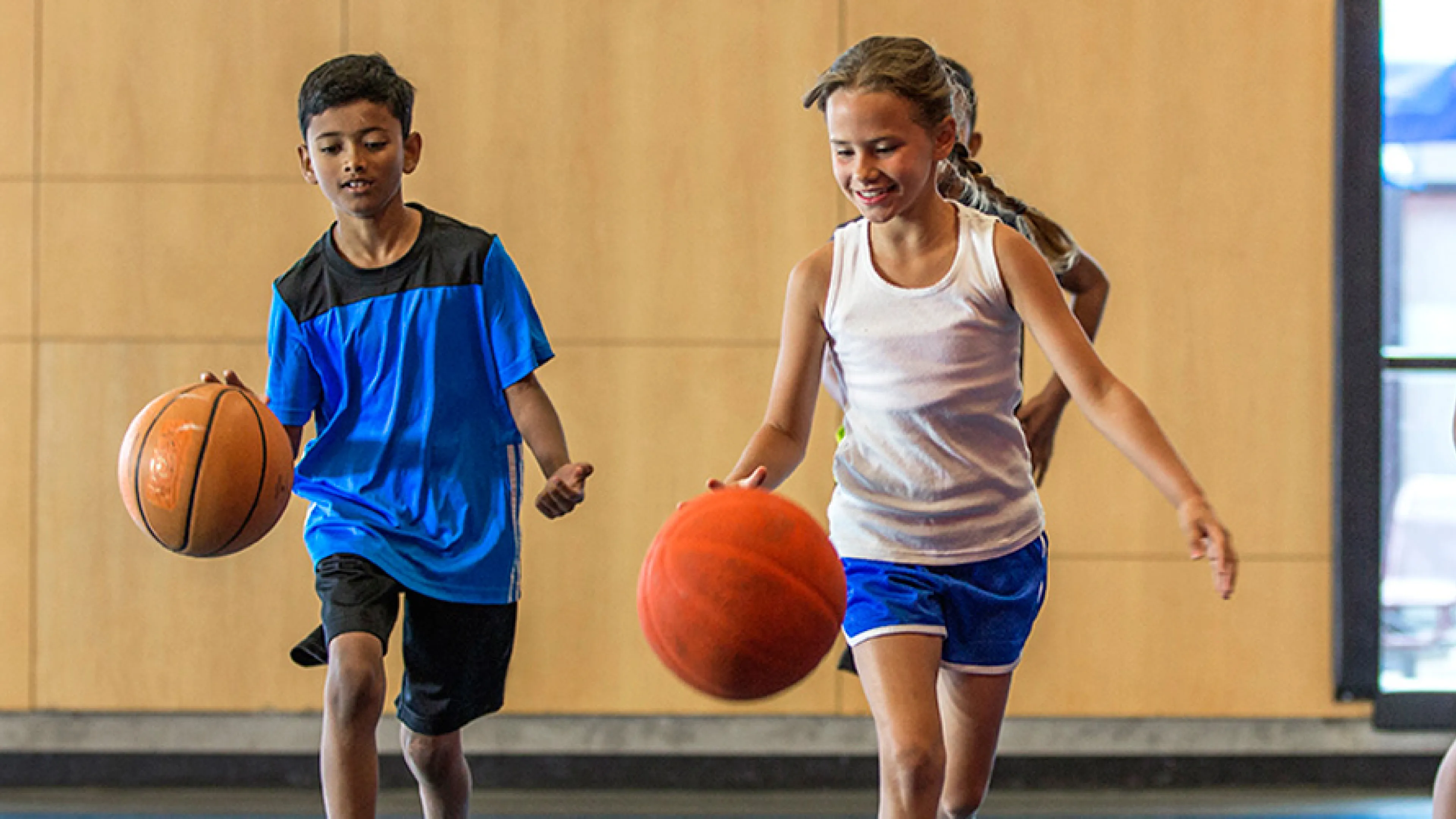 Four school age kids bouncing basketballs in indoor basketball gym.