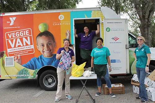 ymca staff holding backpacks in front of veggie van