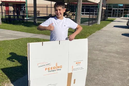 boy stands with feeding tampa bay donation box at the ymca