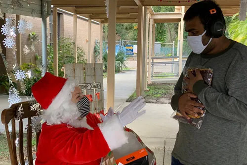 mrs. claus in chair with man wearing mask hugging a gift