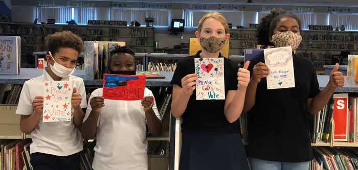 four students holding drawn voting signs in library