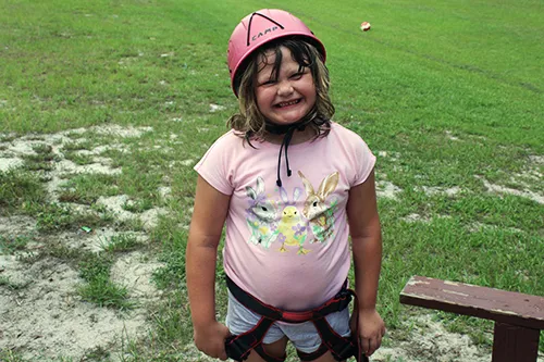 girl wearing climbing gear and helmet outside, grassy background