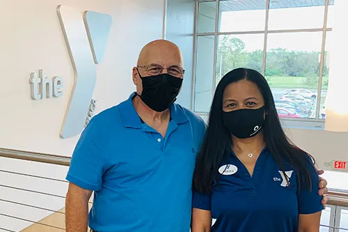 ymca staff member with member inside the YMCA with the Y logo on the wall