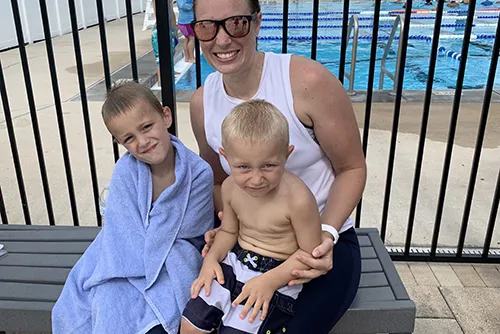 mom and kids at the pool on bench and pool gate behind them