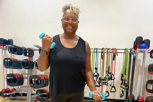 woman wearing black tank top performing bicep curls. weight rack behind her