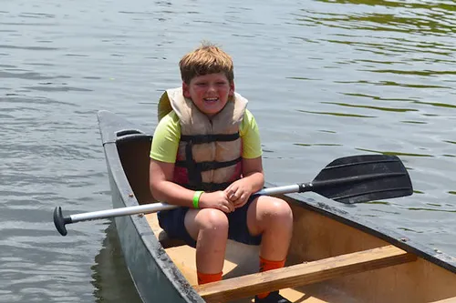 kid wearing lifejacket sitting in canoe on Lake Cristina with oar across his lap