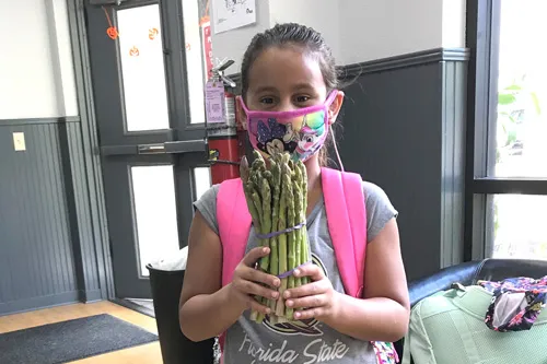 girl wearing a face covering holding the asparagus