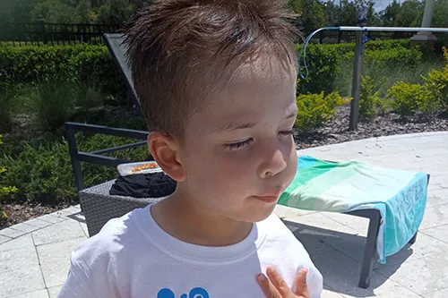 kid wearing shirt on pool deck. lounge chair and towel behind him