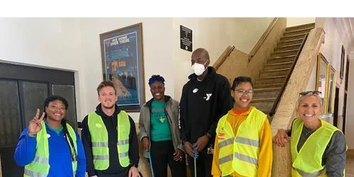 group of six employees wearing yellow vests posing in front of staircase