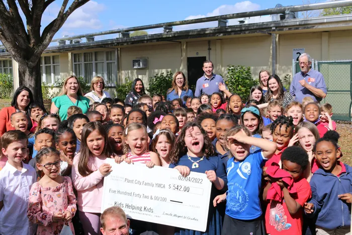thirty elementary school children present check to the YMCA in February 2022 outside of the school 