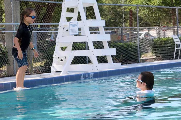 Kid wearing goggles standing on side of pool waiting for swim instructor's directions.