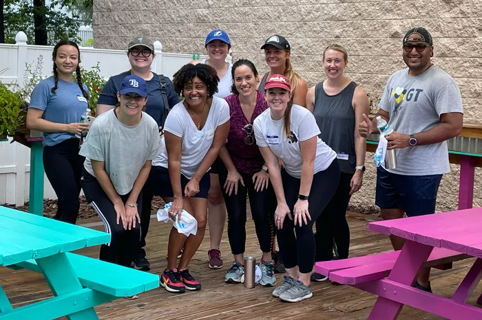 Volunteer group of nine adults pose for a photo on the outdoor deck, where they painted picnic tables.