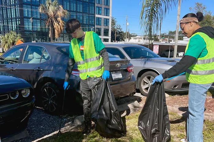 Two teens wearing yellow safety vests looking for trash in a parking lot during the MLK Day of Service 2023 cleanup.