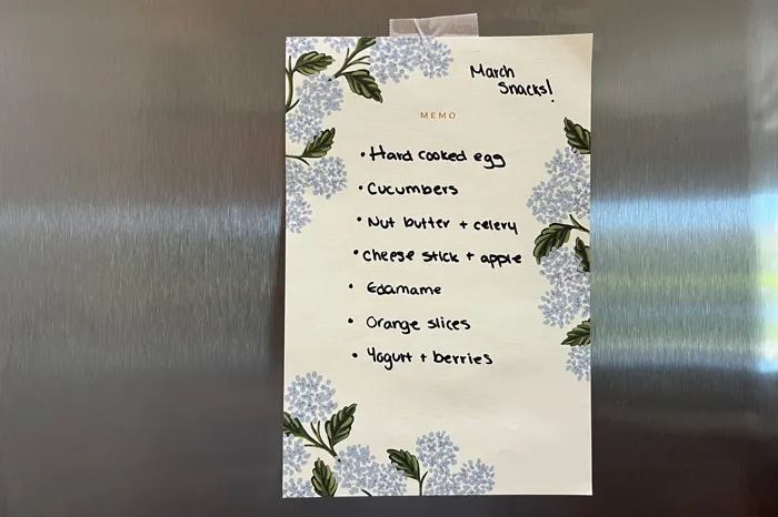 Handwritten list of healthy snacks on stainless steel refrigerator.