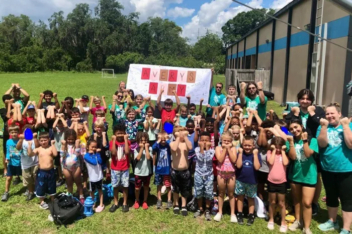 A group of about 50 Plant City Y summer campers and counselors pose for an outdoor photo. Handmade banner in the background reads "Avery's Army" and features signatures from the group's campers.