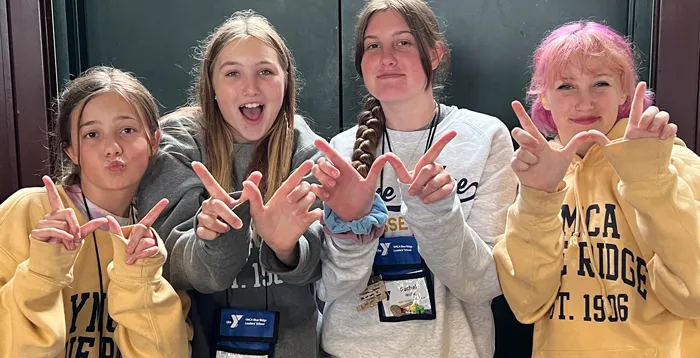 Four female teens wearing sweatshirts and making a W with their own hands pose with smiles.