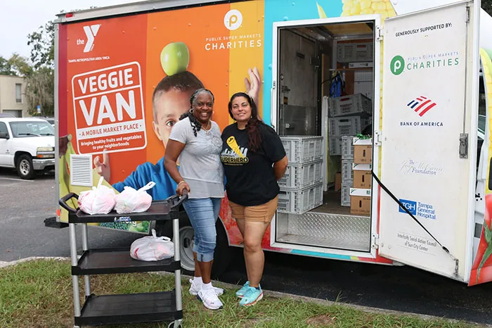 Two women in front of the Veggie Van with food in bags.