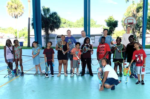 Tampa Y staff volunteers pose kids from Sulphur Springs K-8 Community School students on the tennis court. Kids are smiling and holding rackets after their first tennis clinic.