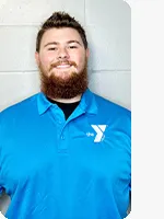 Male personal trainer wearing a blue YMCA staff polo in front of a gray wall.