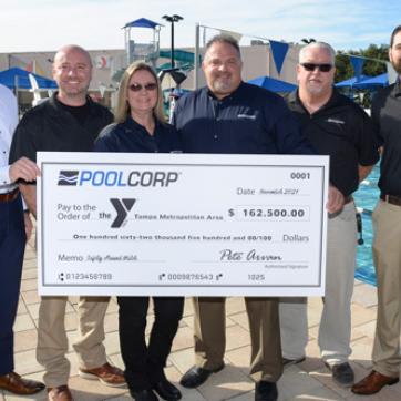 POOLCORP donation check presentation. Four men and one woman representing POOLCORP and Tampa Y CEO Matt Mitchell hold large check on the pool deck at the New Tampa Y. 
