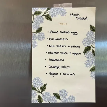 Handwritten list of healthy snacks on stainless steel refrigerator.