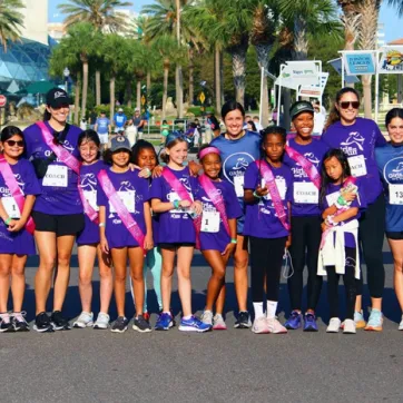 YMCA Camp Cristina Girls on the Run group photo and end of race May 2023. Group is wearing purple shirts in the bright sun – Dali Museum in the background.