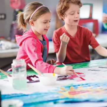 Two children painting on a canvas.