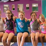 A group of young girls pose on a balance beam.